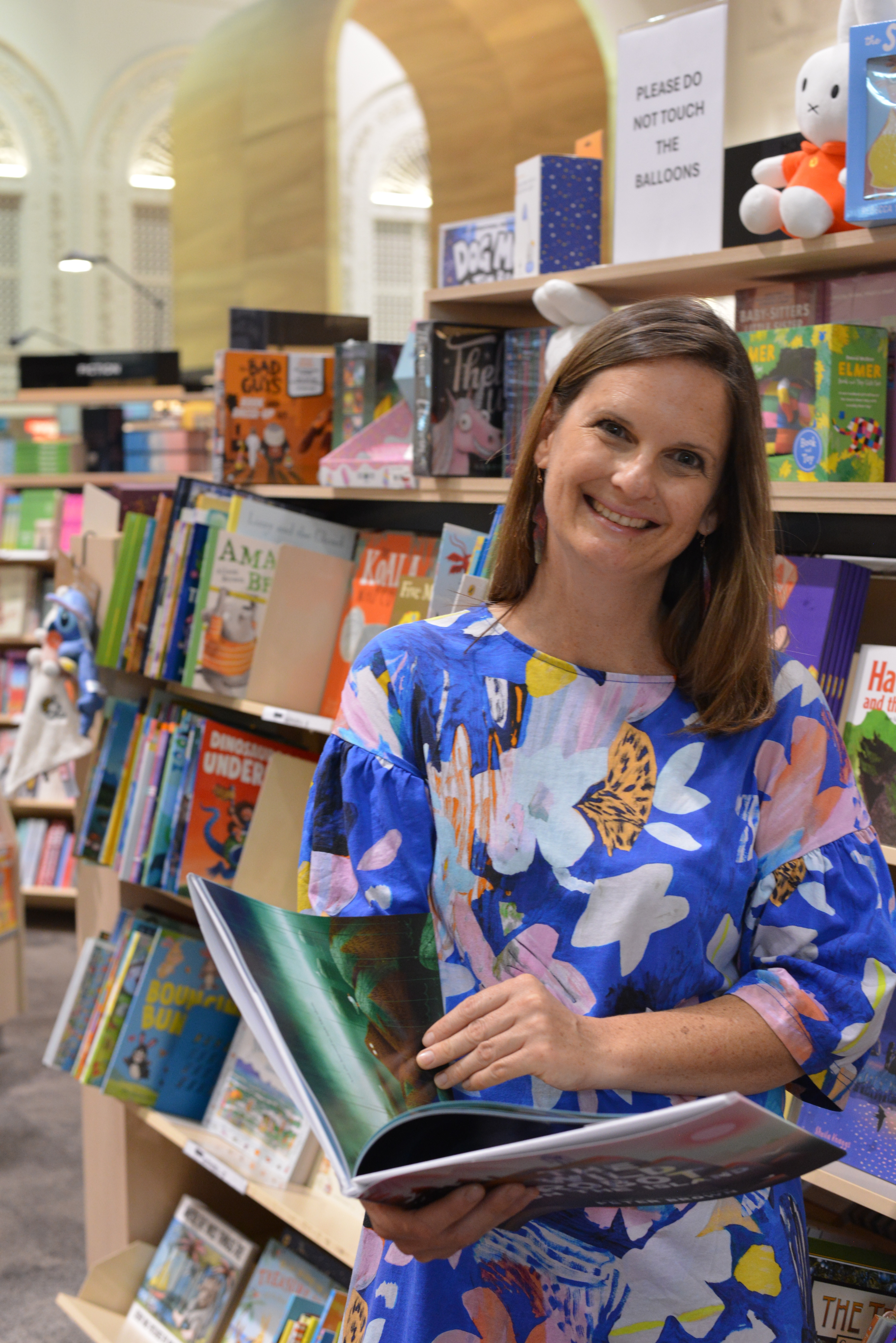 Rebecca Dowd standing in a bookshop holding an open picture book.
