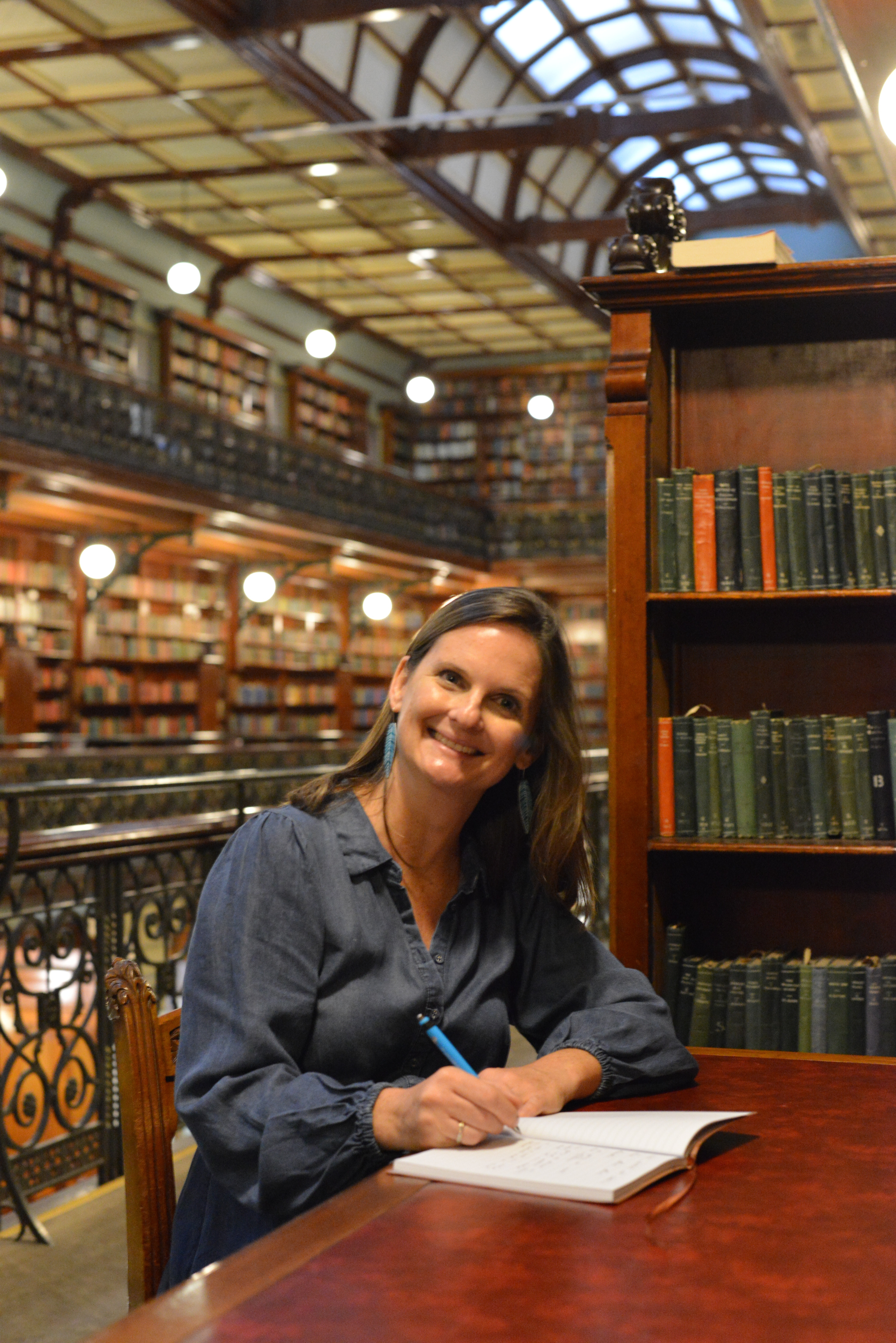 Rebecca Dowd writing in a notebook at a library table.
